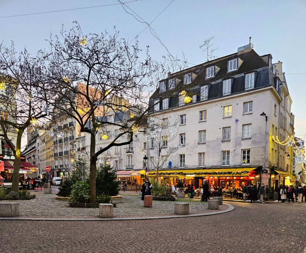 Evening street scene in Paris with warm café lights glowing in the square.